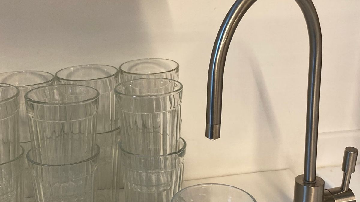 Stainless steel kitchen faucet beside rows of clear drinking glasses