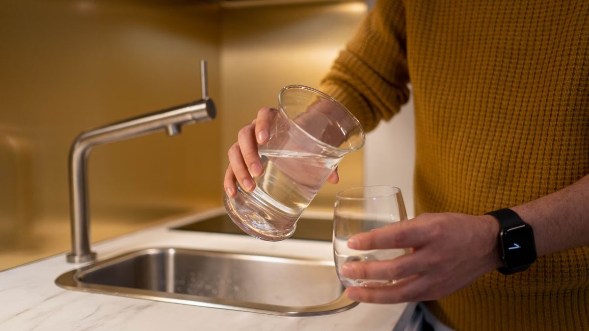 Person filling two drinking glasses at a stainless steel kitchen tap