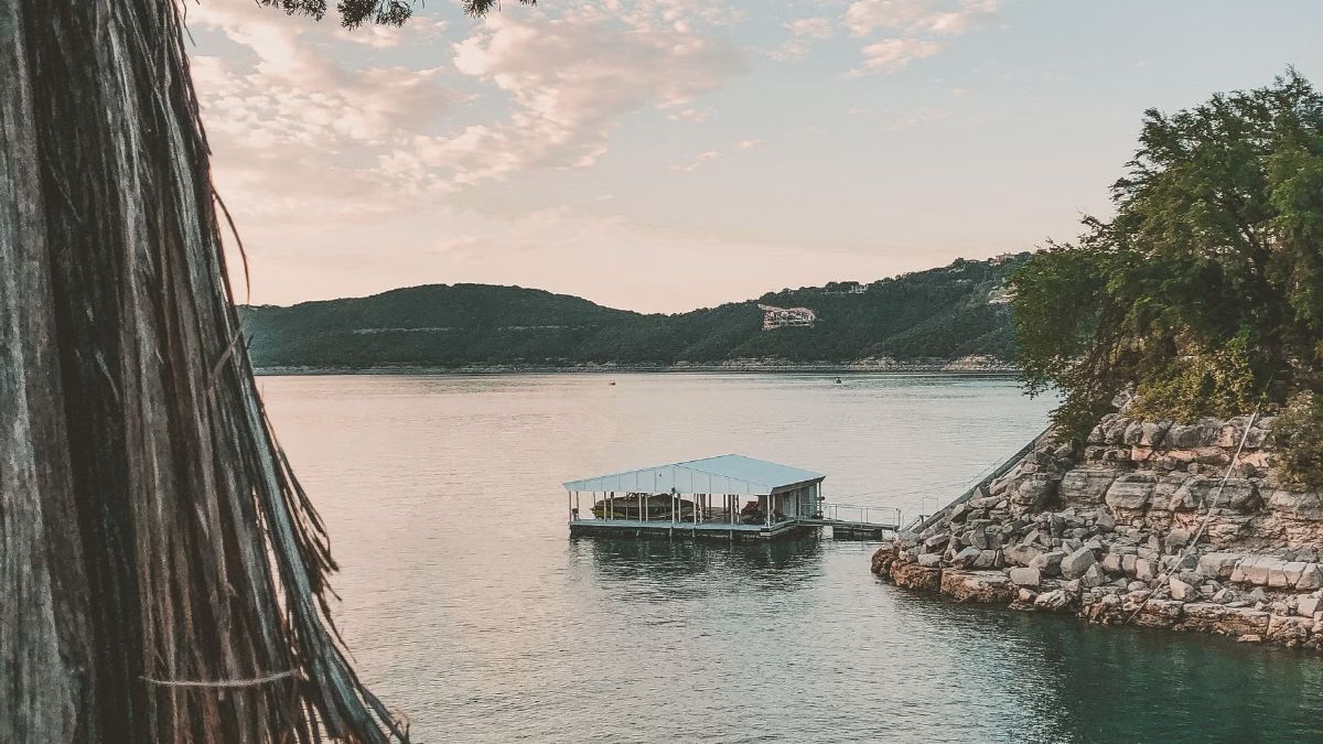 Calm lake with a pale rocky shoreline, trees and a floating boathouse
