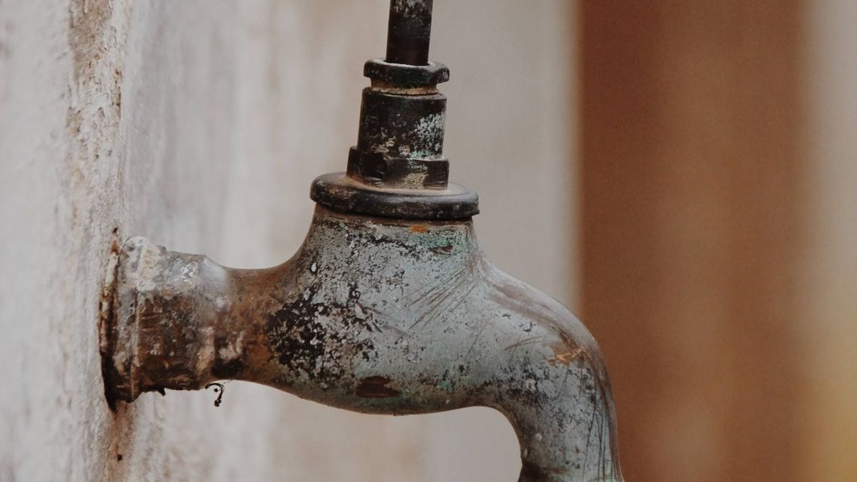 Old metal faucet on a wall, crusted with white and grey mineral deposits