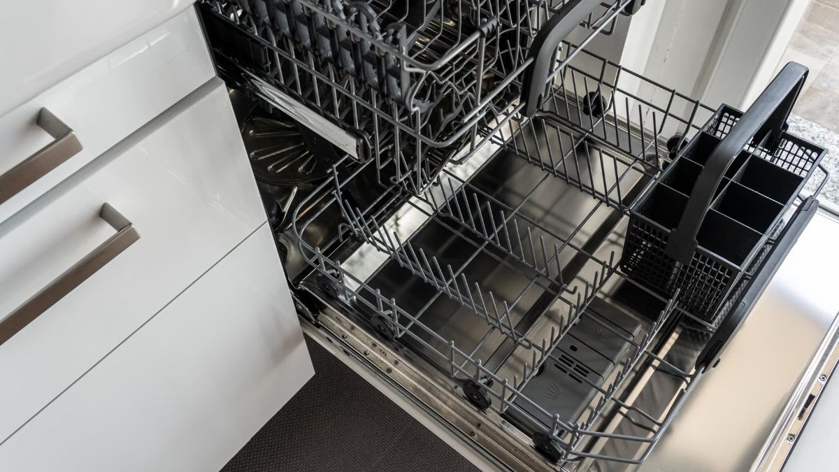 Open empty dishwasher with its lower rack pulled out in a white kitchen