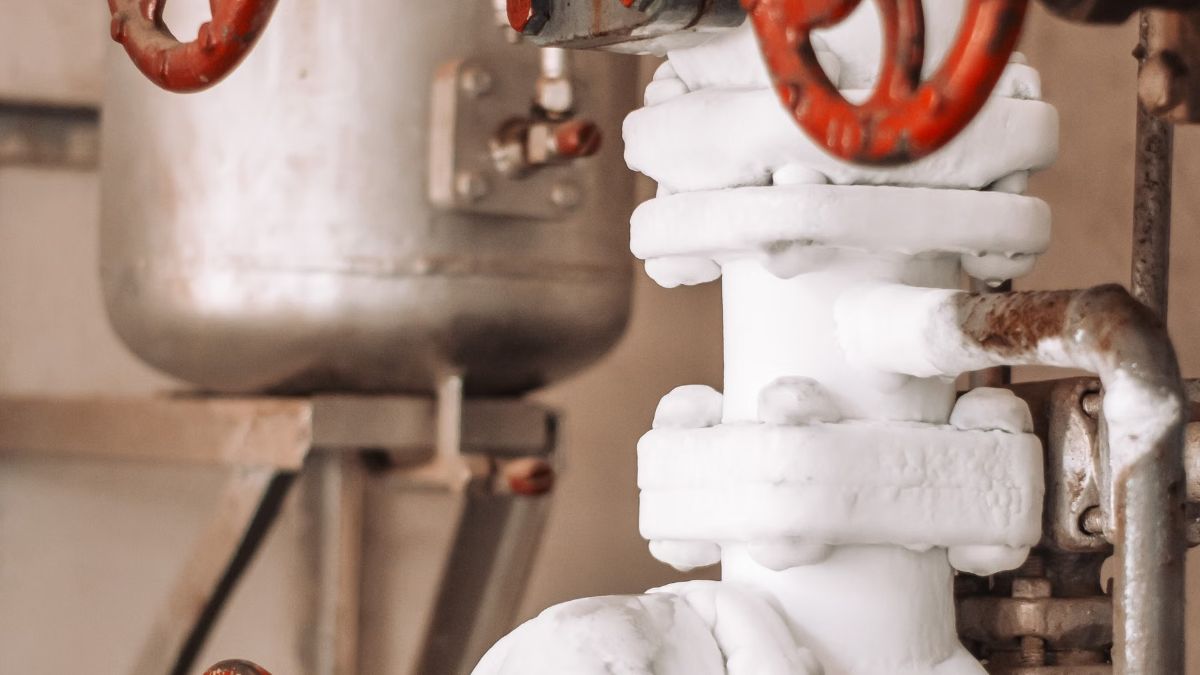 Water pipes with red valve handles and a metal tank in a utility room