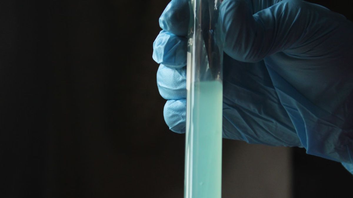 Gloved hand holding a test tube with a pale blue water sample