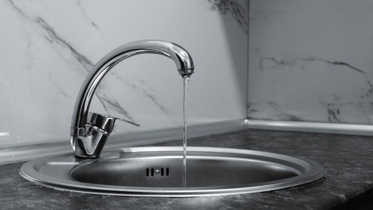 Chrome kitchen faucet running water into a round steel sink